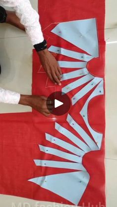 two people are cutting paper with scissors on a red and white table cloth that has the shape of a woman's legs