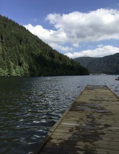 a wooden dock sitting on top of a lake next to a lush green forest covered hillside