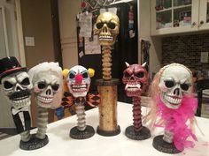 five skulls with different colored hair and makeup on top of a white table in a kitchen