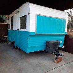 a small blue and white trailer parked in a garage next to a black trash can