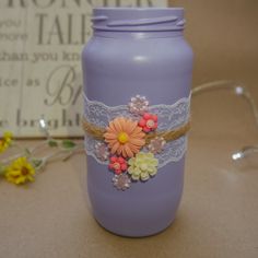 a purple mason jar with flowers and lace on the lid sitting next to a yellow flower