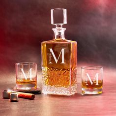 a bottle of whiskey and two shot glasses on a table with the letter m next to it