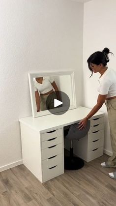 a woman standing in front of a white desk with drawers and a mirror on it