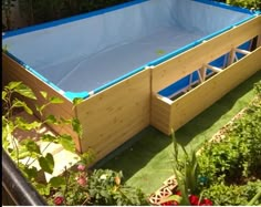 an above ground swimming pool in the middle of some grass and bushes with plants around it