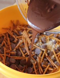 chocolate is being poured into a yellow bowl filled with cookies and pretzel sticks