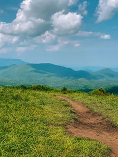 a dirt path on top of a grassy hill with mountains in the backgroud