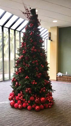 a christmas tree with red balls and greenery in an office building, decorated for the holiday season