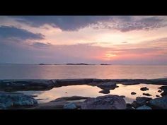 the sun is setting over an ocean with rocks and water in it's foreground