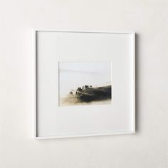 a white frame hanging on the wall displaying an image of a foggy field with trees