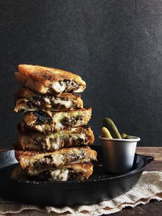 a stack of grilled cheese sandwiches sitting on top of a black plate next to a small cup