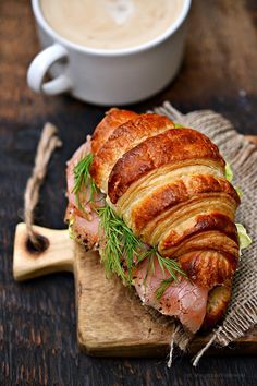 a croissant sandwich with meat and vegetables on it next to a cup of coffee