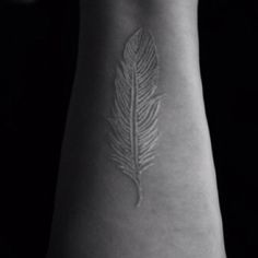 a black and white photo of a person's arm with a feather tattoo on it