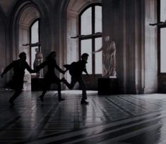 three people are dancing in an old building with large windows and statues behind them on the floor