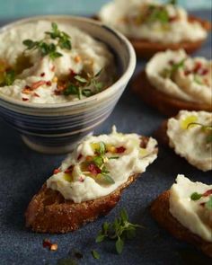 small pieces of bread with cream cheese and herbs on them next to a bowl of dip