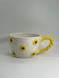 a yellow and white coffee cup with sunflowers painted on the side, sitting in front of a gray background