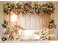 a white couch sitting under a flower covered arch on top of a table next to two chairs