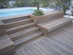 a wooden deck next to a swimming pool with steps leading up to it and plants growing on top