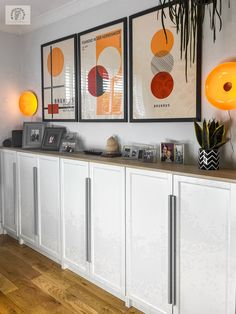 a kitchen with white cabinets and art hanging on the wall above it's counter