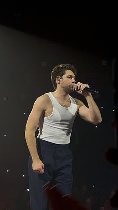 a man standing on top of a stage holding a microphone in his right hand and wearing blue pants