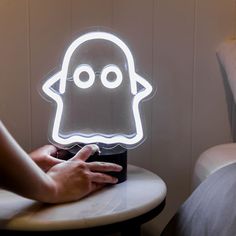 a person holding a glowing ghost shaped light up on a small table with a bed in the background