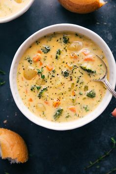 a bowl of soup with broccoli, carrots and bread on the side