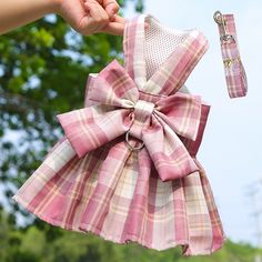 a hand holding a pink and white plaid dress with a large bow on it's back