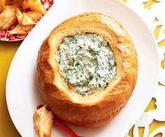 a bowl of spinach dip in a bread bowl on a plate next to french fries