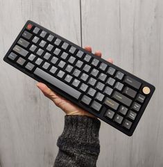 a person holding a black keyboard in their left hand, with white keys on it