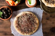 an uncooked pizza sitting on top of a table next to bowls of vegetables