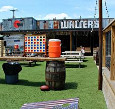 an outdoor play area with wooden barrels and american flags on the grass in front of a building