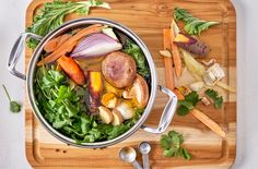 a pot filled with vegetables on top of a wooden cutting board next to utensils