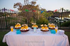 a table topped with cakes and drinks on top of a white cloth covered tablecloth