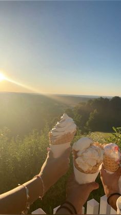 two people holding ice cream cones in their hands while the sun shines brightly behind them