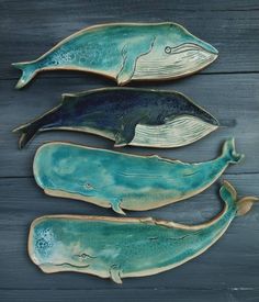 three ceramic whales sitting on top of a wooden table next to each other, one blue and the other green