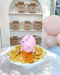 a pink pig sitting on top of a pile of gold coins in front of balloons