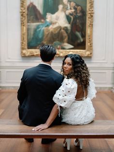 a man and woman sitting on a bench in front of a painting