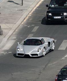 a silver sports car driving down a street next to two black cars on the road