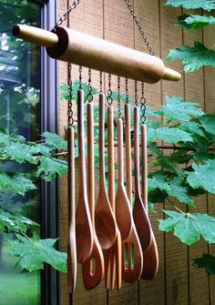 several wooden spoons hanging from a chain in front of a window with green leaves