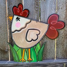 a painted chicken sitting on top of green grass next to a wooden fence with hearts