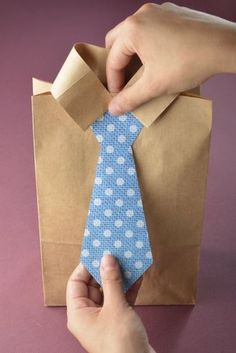 a person tying a blue tie on top of a brown paper bag with white polka dots