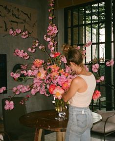 a woman standing in front of a vase filled with pink and red flowers on top of a wooden table