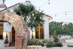 a house with lights strung from the roof and palm trees in pots on the front yard