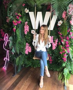 a woman sitting on a swing in front of a floral wall with the letter w