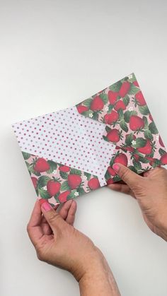 two hands are holding an envelope that has strawberrys on it and polka dot paper