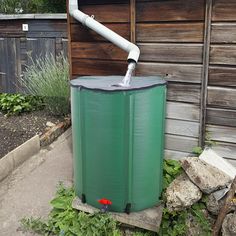 a green water heater sitting in front of a wooden building next to rocks and plants