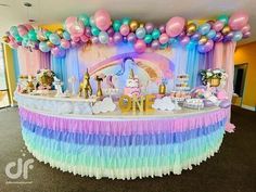 a table topped with lots of balloons and other items next to a rainbow colored wall