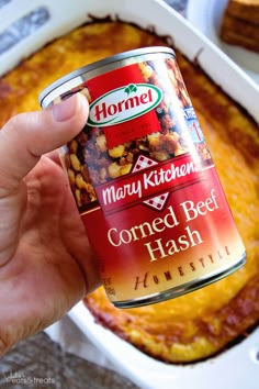 a person holding up a can of corned beef hash browns in front of a casserole dish