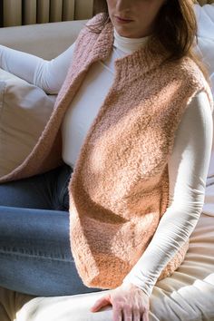 a woman sitting on top of a couch wearing a pink knitted sweater and scarf