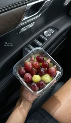 a person holding a plastic container filled with grapes in the passenger seat of a car