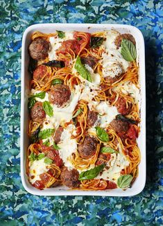 a casserole dish filled with meatballs and sauce on a blue floral tablecloth